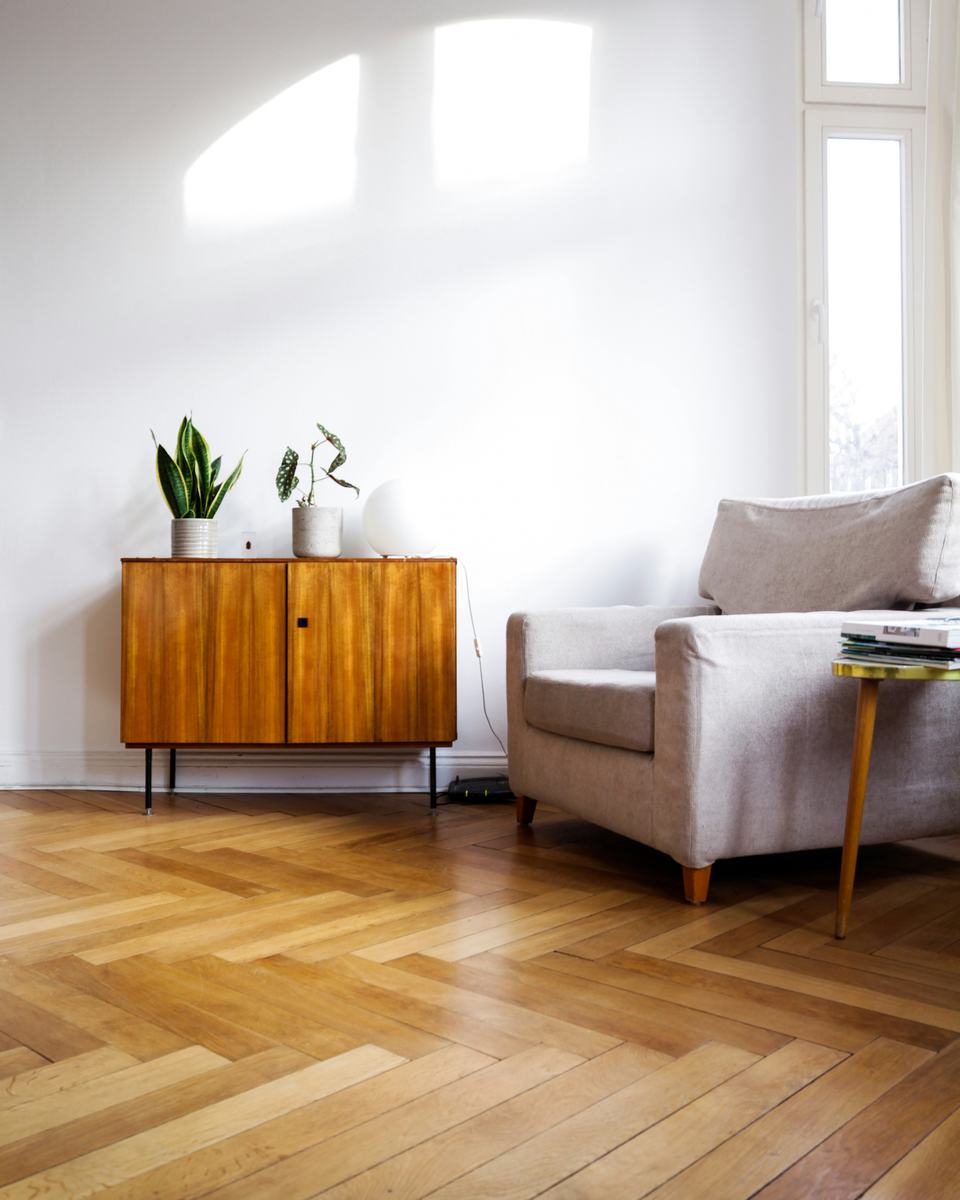 Fischgrätparkett in einem Wohnraum, Sideboard und Sessel im warmen Tageslicht