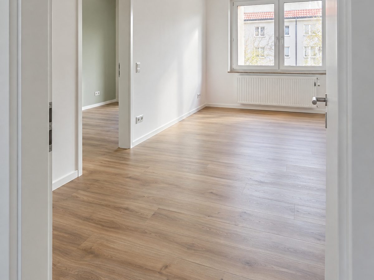 Leere, frisch renovierte Wohnung mit durchgehendem Eichenboden, weißen Wänden und Blick durch offene Türen